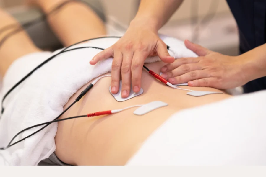 Fisioterapeuta aplicando electroestimulación y técnicas manuales en la espalda de un paciente
