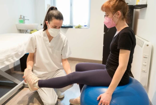 Fisioterapeuta realizando ejercicio de rehabilitación con paciente sobre pelota de pilates en clínica digital