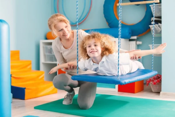 Fisioterapeuta realizando terapia de integración sensorial con niño con autismo en sala de fisioterapia infantil