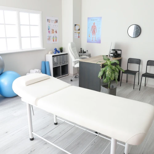 Clínica de fisioterapia moderna con camilla, pelota de pilates y zona de recepción organizada
