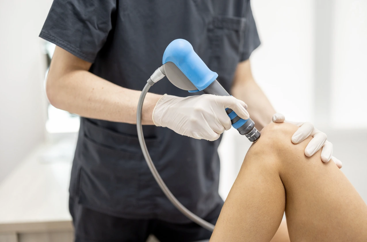 Fisioterapeuta aplicando terapia con ondas de choque en la rodilla de un paciente